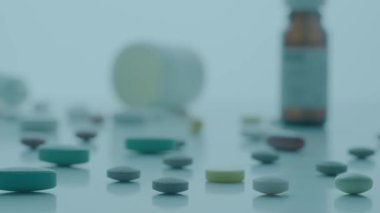 Mavi arka plandaki masaya saçılmış yuvarlak ve oval haplar. Tabletler ve çeşitli tıbbi şişelerle birlikte masanın üzerinde kamera hareketi. Vitaminler, antibiyotikler ve ağrı kesicileri kapatın. Tıp kavramı