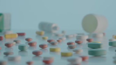 Tabletler ve çeşitli tıbbi şişelerle birlikte masanın üzerinde kamera hareketi. Yuvarlak, oval, sarı ve kahverengi haplar mavi arka plana saçılmış. Vitaminler, antibiyotikler ve ağrı kesicileri kapatın.