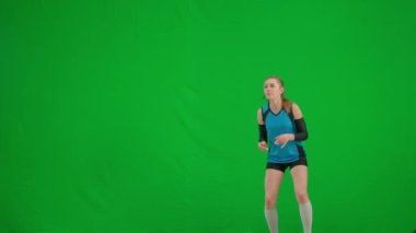 Genç bir kadın zıplıyor, topa vuruyor ve yere düşüyor. Yeşil ekran krom anahtarında voleybol oynayan bir sporcu. Yarışmada voleybolcu kadın oyuncu mavi ve siyah spor giydi.