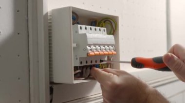 Elektrikçi elektrik panelini monte eder. Tornavidayla vidayı sıkan ve santraldeki yüksek voltajlı elektrik düğmelerini açan bir adamın ellerini kapatın. Otomatik sigortalı kutuyu değiştir