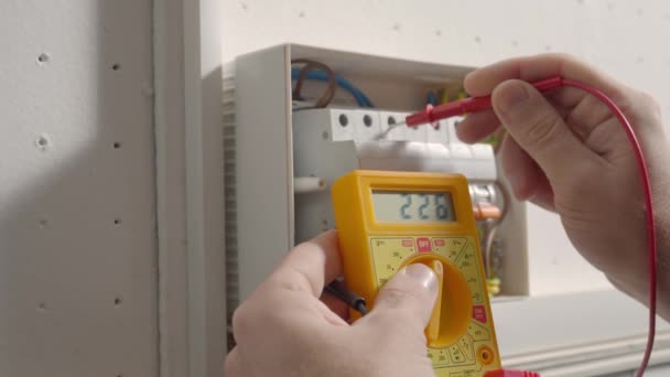 電圧下で動作し 電気技師は黄色のマルチメータで電圧を測定し 機器の保守性をチェックしています ホワイトスイッチボックスチェック電圧スイッチボードをテストする人の手を閉じる — ストック動画