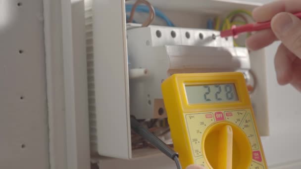 電圧下で動作し 電気技師は黄色のマルチメータで電圧を測定し 機器の保守性をチェックしています ホワイトスイッチボックスチェック電圧スイッチボードをテストする人の手を閉じる — ストック動画