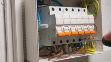 Elektrikçi elektrik panelini monte eder. Yüksek voltajlı elektrik düğmelerinde tornavidayla vidayı sıkan adamın ellerini kapatın. Otomatik sigortalı, kablolu, anahtarlı kutucuğu değiştir