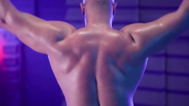 Gövdesi çıplak, erkek vücut geliştirici. Koyu renk spor salonunda kafasının arkasından halteri kaldırıyor. Mavi ışıkla. Şişkin kasları olan bir adam sırt, deltoid ve kol kasları için egzersiz yapıyor. Kapat