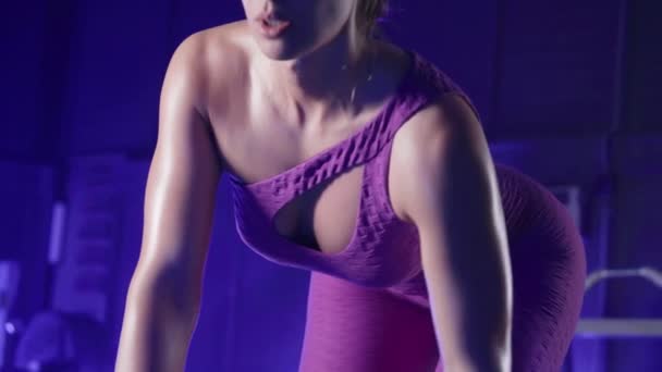 紫のスポーツの運動能力の女性は 全体的に傾きの推力ダンベルを行います 後部のDeltoidと腕の筋肉をポンプスポーツ女性 青色の光を持つジムで運動する女性ボディービル — ストック動画