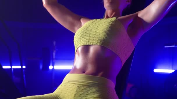 女健美运动员举起杠铃 做肩部运动和呼吸 穿着黄色运动服的运动健美女子在昏暗的蓝光体育馆里锻炼 武器和腹部的近距离接触 — 图库视频影像