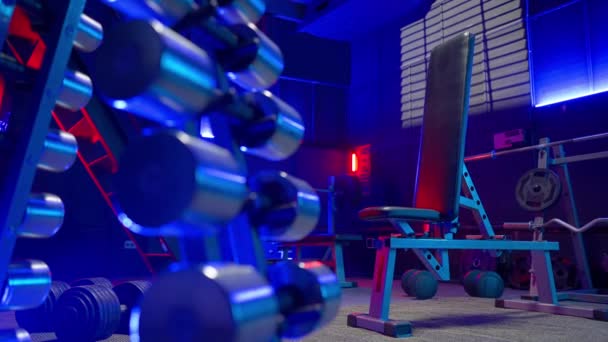 在一个有蓝灯和红灯的空体育馆里 用哑铃 杠铃和重物 运动长椅和茶壶敲打 举重等方面的运动器材 — 图库视频影像