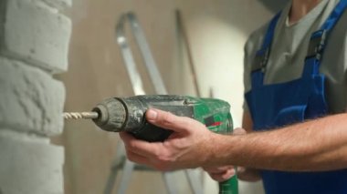 Erkek müteahhit delgiyle ya da elektrikli matkapla beyaz tuğla duvar deliyor. Mavi üniformalı bir adamın duvarda delik açmasına yakın durun. Tamir konsepti, inşaat, tedarik