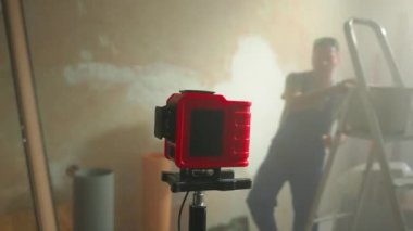 Mavi önlüklü ve gözlüklü adam kırmızı lazer ruleti yanıp sönen yeşil ışınla ayarlıyor. Kesişen yeşil lazer mezura demeti kahverengi duvarda sergileniyor. Yenilenmekte olan oda