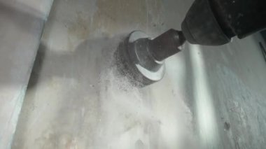 Gri beton bir duvara soket deliği açmak. Yuvarlak başlıklı bardak elektrikli matkap ya da delgi üzerinde dönüyor. Matkapla delme işlemi sırasında alçıdan çıkan beyaz toz ufalanır. Kavram
