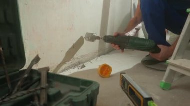 Mavi üniformalı adam soket için beton duvarda delik açıyor. İnşaatçı döner elektrikli matkap ya da delgi ile delik açar. Alçı parçalarından beyaz toz. Konsept