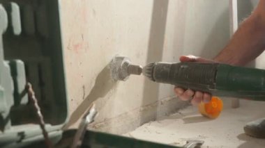 Bir adam soket için beton duvarda delik açıyor. İnşaatçı döner elektrikli matkap ya da delgi ile delik açar. Alçı parçalarından beyaz toz. Tamir, inşaat, yeniden yapılanma kavramı