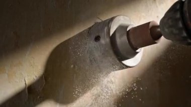 Yuvarlak metal başlık, soket için duvarda bir delik açar. Dönen başlıklı bir performans, ışık demetinde makro atış. Duvarı delme işlemi sırasında, beyaz alçı parçacıkları