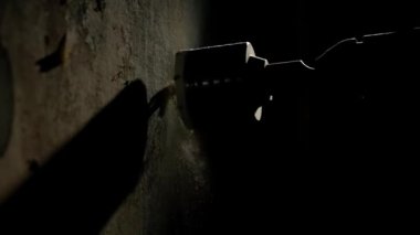 Karanlıkta ışık huzmesi ile duvarda delik açmak için makro atış. Elektrikli matkap veya delgi üzerinde dönen metal yuvarlak hortum kapağının yan görüntüsü. Beyaz tozu delme işlemi devam ediyor