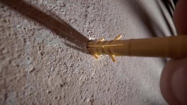 İnşaatçının parmaklarının duvardaki delinmiş bir deliğe sarı plastik bir panel sokarken makro görüntüsü. Bir işçi ağır metal bir çekiçle duvarda bir delik açıyor. Düşük görünüm açısı