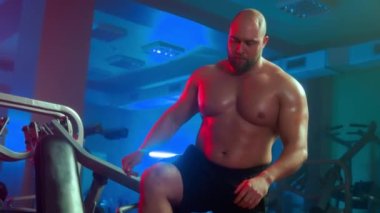 Male bodybuilder is stringing black round weights on sports equipment. Athlete is sitting on sports simulator and performing the arm press technique. Man is pumping up muscles of chest and deltas in