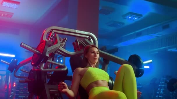 身穿黄色运动服的女健美运动员正坐在运动模拟器上 运用手臂按压技术 女人在体育馆里用红色蓝光抽吸胸部和三角洲的肌肉 — 图库视频影像