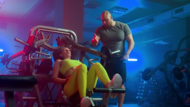 男教练员正在教女人正确的技巧 让她们在运动模拟器上进行伸展运动 身穿黄色运动服的女健美运动员坐在机器上做运动 — 图库视频影像