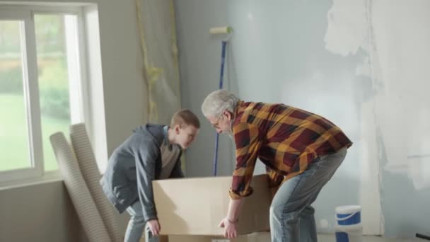 Grandpa Grandson Carrying Heavy Cardboard Box Placing Floor Window Elderly — Vídeos de Stock