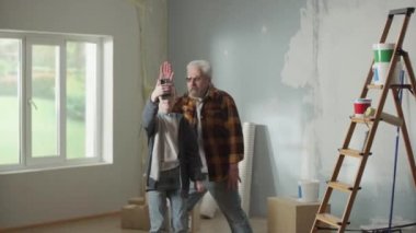 Grandpa and grandson are talking on video call using a mobile phone. A young guy is talking, waving hello and an older man is clinging over a stepladder that is falling. Concept of repair in apartment