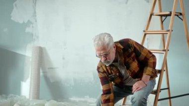 Tired elderly man is sitting on a ladder and calling a master to repair an apartment using a mobile phone. Aged pensioner is rejoicing at idea and solved problem with help of the master. Concept of