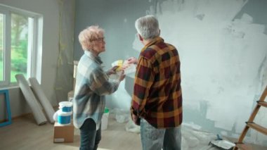 Elderly man and woman are choosing paint color on color palette. Aged couple is discussing color of wall painting, during renovation of apartment, rear view. Concept of repair, decoration, interior