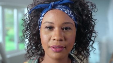 Young African American woman looking at camera and smiling. Portrait of black female with curly hair in checkered shirt posing against the backdrop of an apartment in process of renovation. Concept of