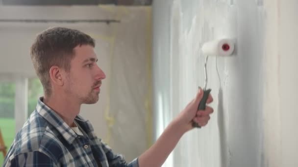 Młody Człowiek Maluje Ścianę Białą Farbą Pomocą Wałków Malarskich Tle — Wideo stockowe