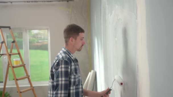 Молодой Человек Рисует Стену Белой Краской Помощью Роликов Краски Фоне — стоковое видео
