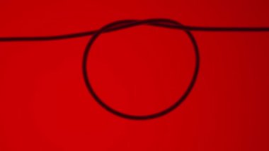 Hair that is tied into a round loop on a red background. Macro shot of a thin even hair tied into a knot and forming a circle. Texture of human hair. Thread, string, hair under a microscope or