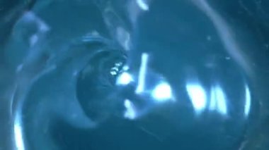 The surface of clear blue water swirls into a whirlpool and a funnel is formed. Swirl of a transparent liquid. Draining water, leaking in the bathroom or sink. A round hole from a water vortex is