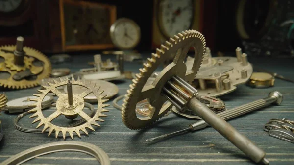 Disassembled watch parts, clockwork. Metal gears, toothed wheels, cogwheels, gearwheel against blurred background of many vintage table clocks. Broken old clock and a screwdriver in the workshop
