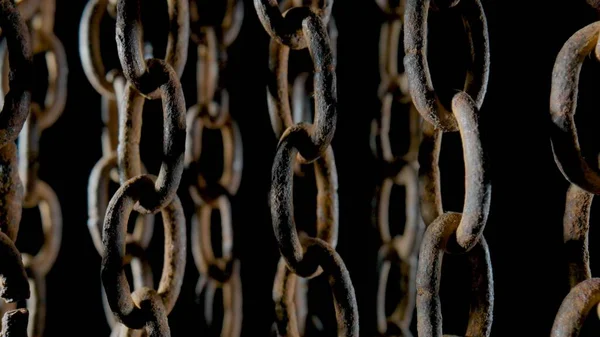 Rusty metal old chain dangling in dark indoor space. Close up of the links of an aged iron chain covered with corrosion and dust. Rough damaged metal structure. Grunge. Strong uneven metal connections