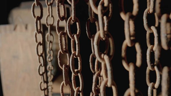 Rusty metal old chain dangling in dark indoor space. Close up of the links of an aged iron chain covered with corrosion and dust. Rough damaged metal structure. Grunge. Strong uneven metal connections