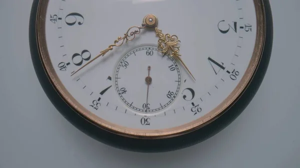 Antique pocket watch with a white dial and gold second, minute and hour hands on a light gray background. The face of an old clock with numbers close up. Round mechanical vintage pocket watch