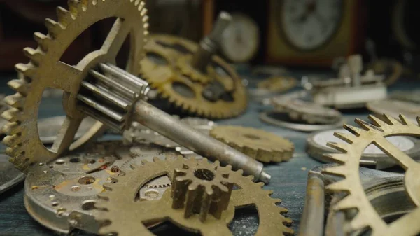 Pile of metal internal parts of an old clock. Clockwork, gears, cogwheels lie on the table on a blurred background of vintage clocks. Disassembled clock mechanism of an old watch. Clock parts in the