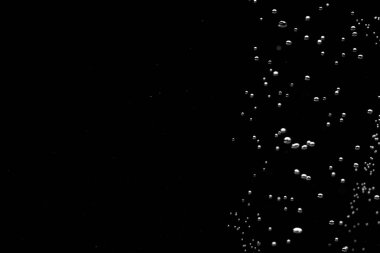 Shiny air bubbles in the right side of the frame on a black isolated background. Background with oxygen bubbles and workspace, mockup. Close up of a bubbling liquid. Fizzy flow of air bubbles