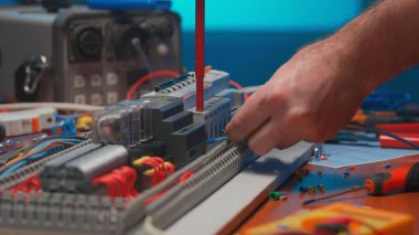 Unrecognizable man with a screwdriver in his hands twists the blue wire in an automatic electrical switch in an electrical workshop. An electrician is repairing a switchboard with switches. Close up