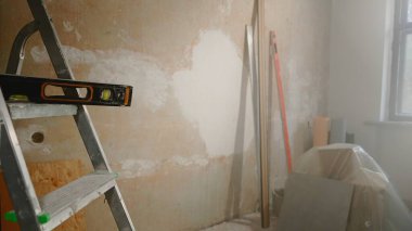 Black level lying on metal ladder against brown wall. The interior of the room inside in the process of renovation or construction work. Cardboard boxes are covered with polyethylene. Measuring