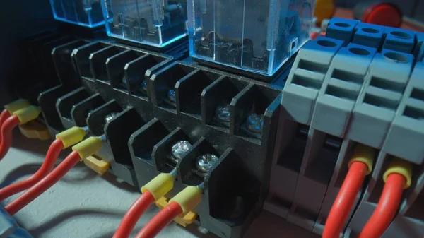 Gray plastic electrical panel with many red wires, yellow bushing ferrules screwed to the panel, electrical parts, automatic switches, breakers. Close up of a high voltage electrical switch on a table