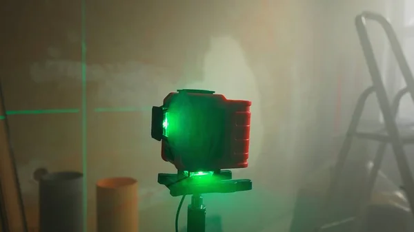 Green beam of red laser roulette is displayed on brown wall. Lines are intersecting and indicating the location of the mark. Level measurement with a laser ruler. Room under renovation with ladder and