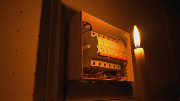 High voltage automatic breaker switch, close up in the dark. Candle illuminates a white electrical panel with many wires, automatic switches, breakers, residual current devices, fuses. Blackout