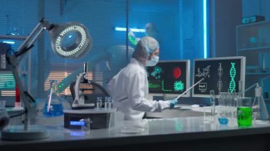 Tıbbi gelişim laboratuvarı. Kadın bir bilim adamı klavyeye yazar ve araştırma verilerine girer. Modern bir laboratuvarın arka planına karşı deney tüpleri, mataraları ve...