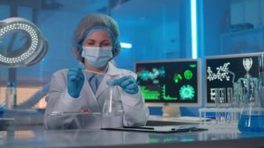 Kadın bir bilim adamı mataradaki temiz bir sıvıya kahverengi toz ekler. Kadın örneğin tepkisini gözlemliyor, sıvıyı karıştırıyor ve test verilerini yazıyor. Modern bir biyokimya laboratuvarında araştırma