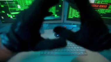 Hacker stretching hands in black gloves and typing on a computer keyboard, hacking password. Computer screen with green program codes. Access denied, access granted. The spy copies the files to the
