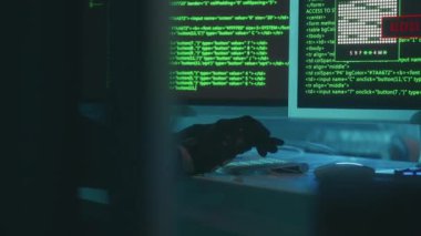 Hacker is typing on a computer keyboard and cracking a password. A man in a black hoodie and gloves is hacking security systems. A green line of codes appears on the screen. Access denied, then to