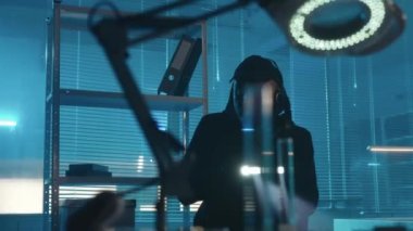 A hacker in a black hoodie and gloves is spying in the laboratory, typing on a computer keyboard. A man downloads a virus to computer and the infection rate starts counting down. The source code and a