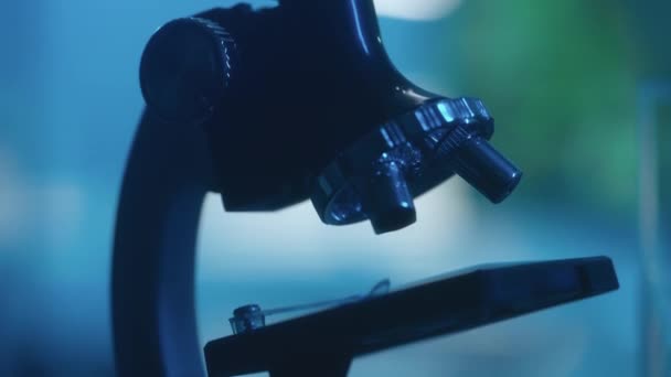 相机在一个带有柔和蓝光的黑暗实验室里穿过显微镜 带有镜头 三脚架 目镜和左轮手枪的实验室设备都非常接近 生物研究显微镜 可以吗 — 图库视频影像