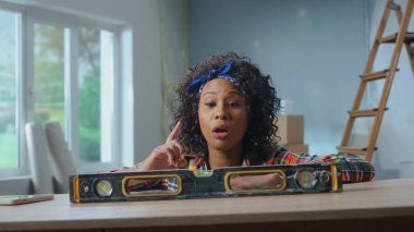 A young African American woman poses next to a building bubble level on a table. A black woman is thinking about something and she has an interesting idea. Concept of repair, finishing works, interior