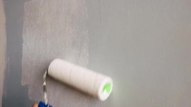 The unrecognizable man paints a gray wall with white paint using a paint roller. Close up of a painters or repairmans hand sliding a roller over a wall and painting over it. The concept of repair